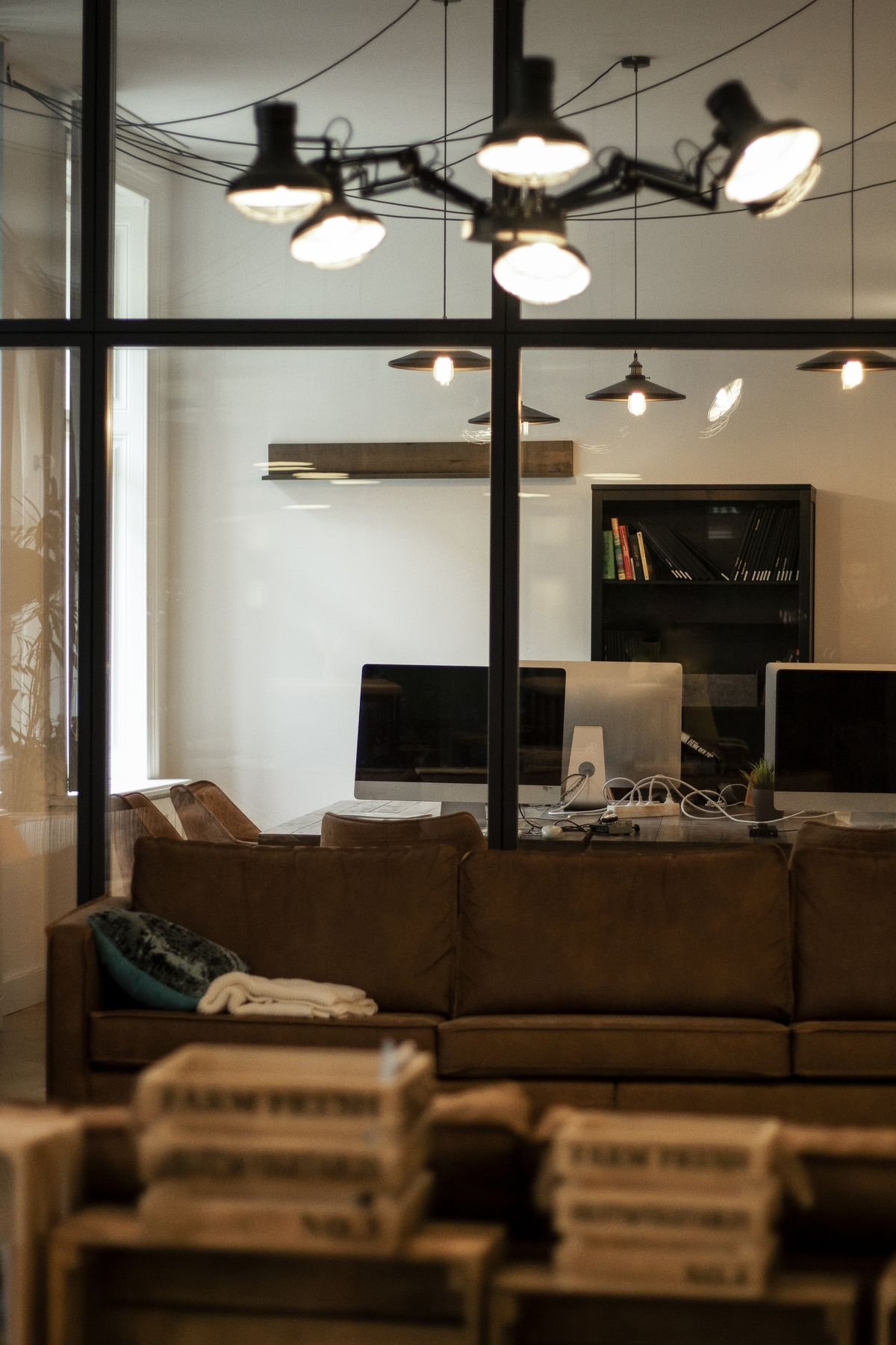 A warm office interior seen through steel-framed glass, with leather seating and pendant lighting