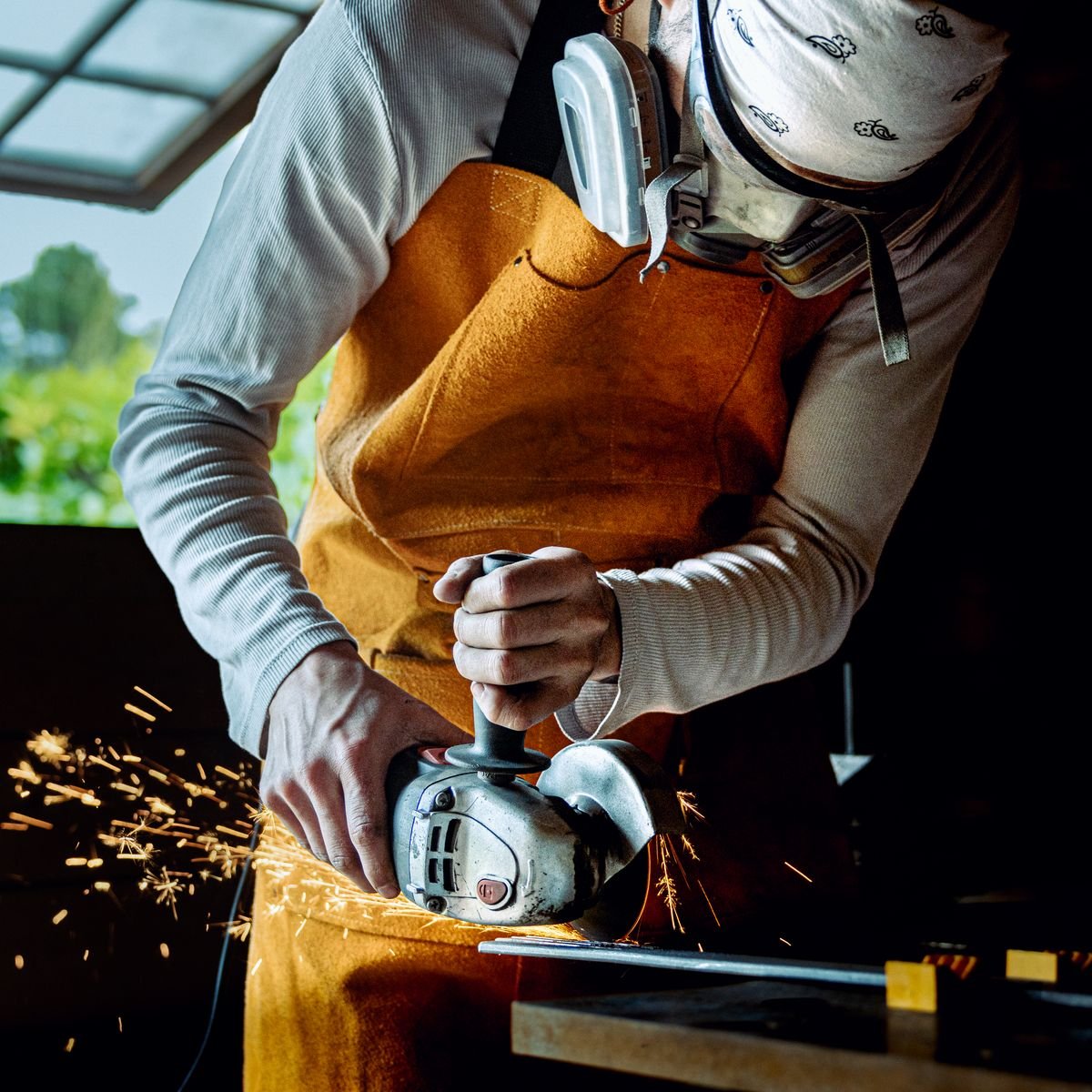 A tradesperson in a leather apron working an angle grinder in a workshop