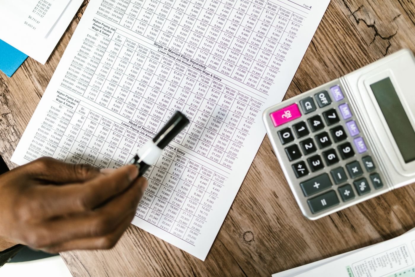 A hand marking a printed tax table beside a calculator