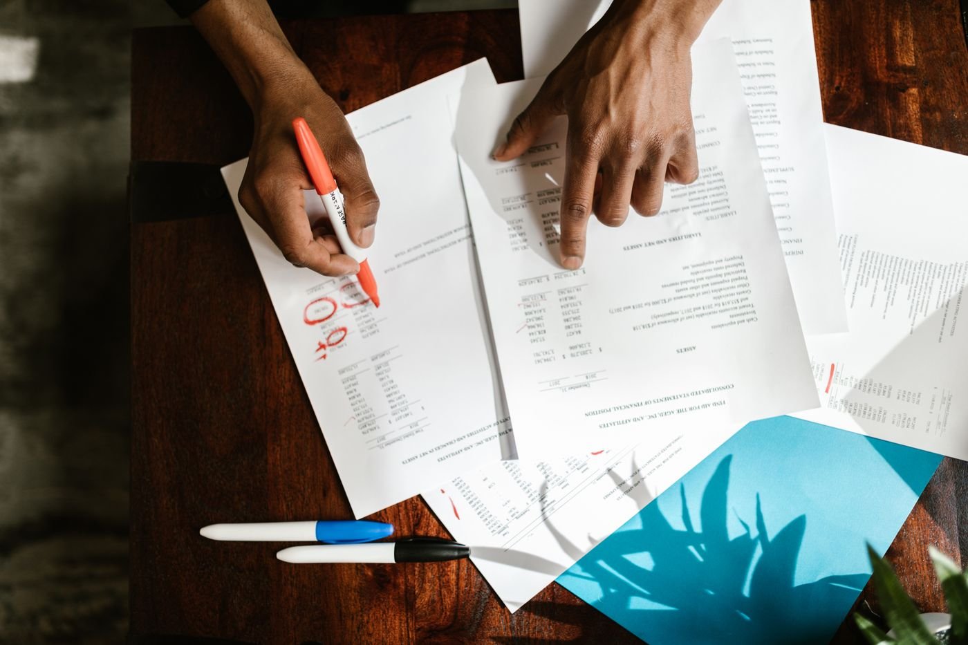 Hands working across printed statements on a dark timber desk