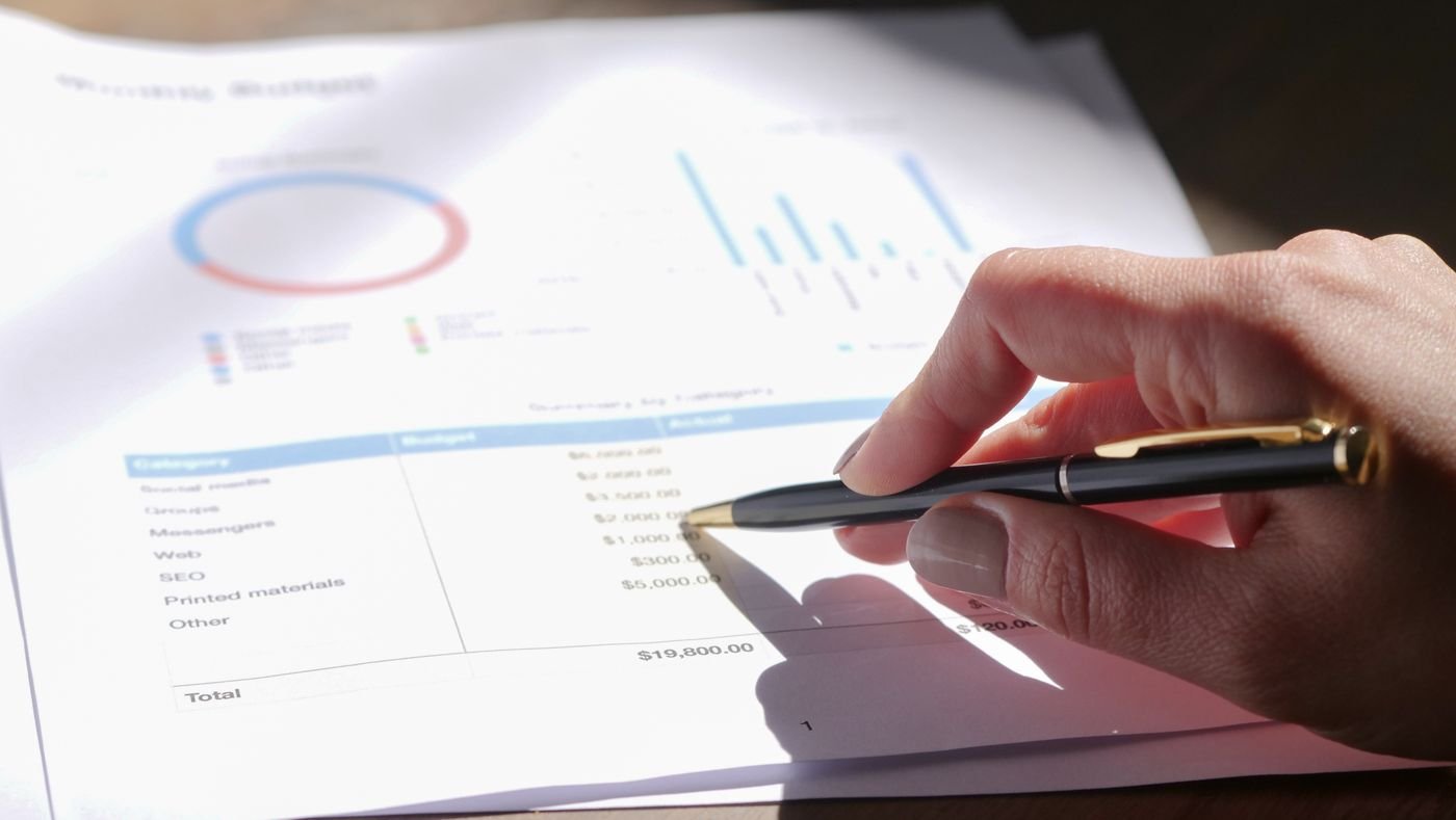 A hand annotating a printed budget summary with a fountain pen
