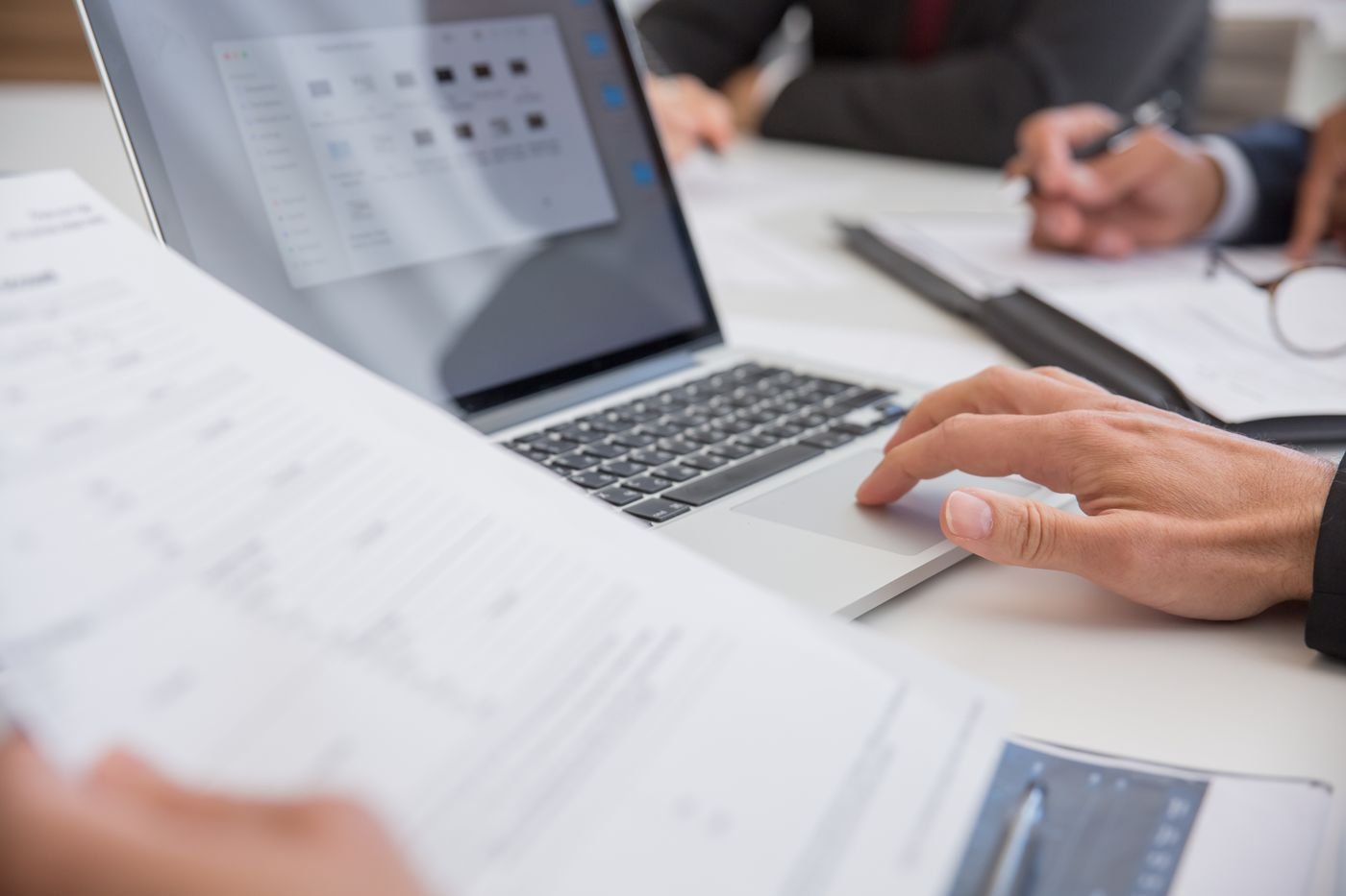 A laptop open on a desk beside printed reports during a working session